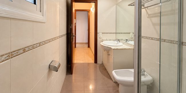 Baño moderno con puerta abierta y ducha de cristal